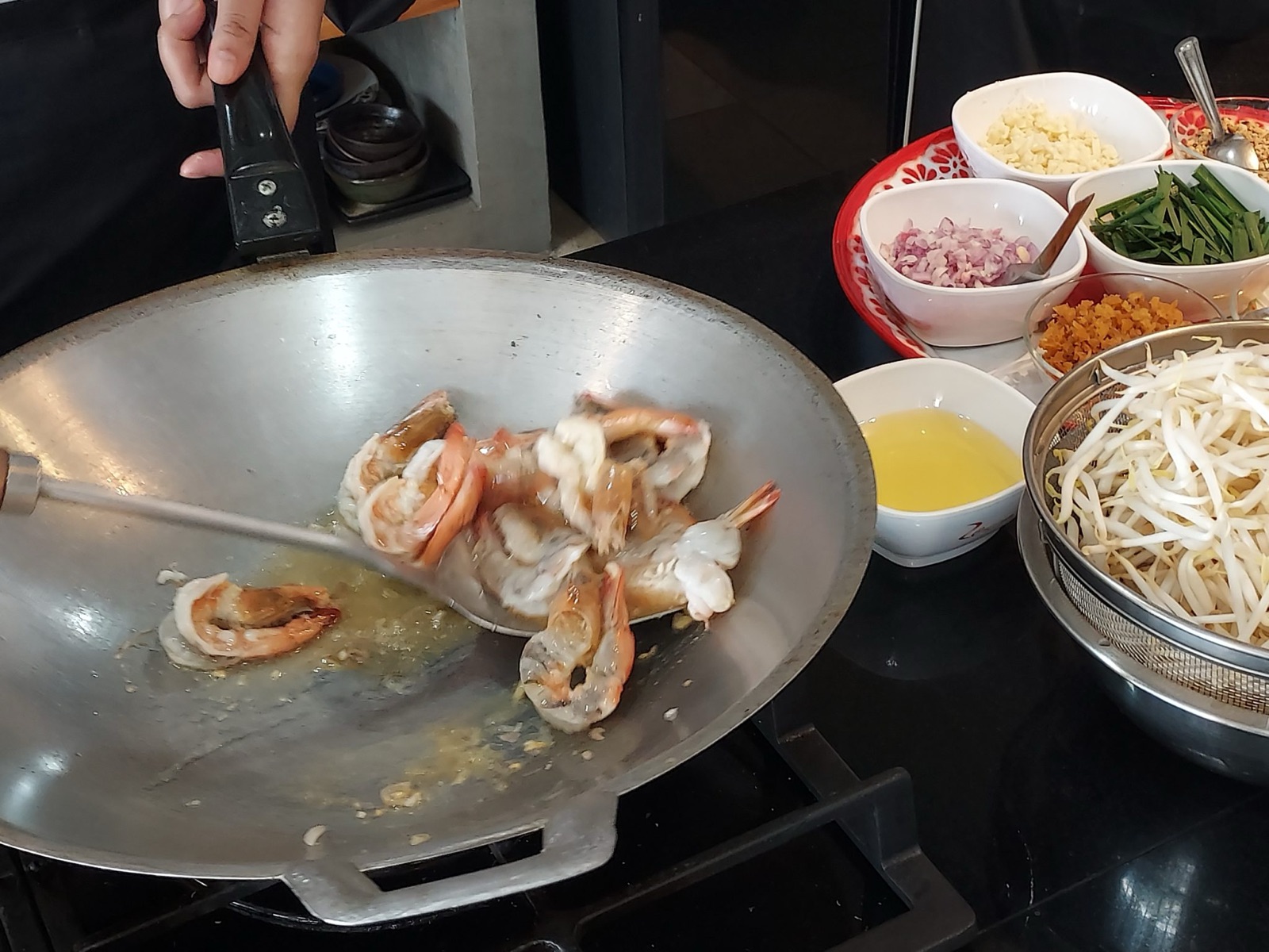 ผัดกุ้งในกระทะเหล็ก รายล้อมด้วยเครื่องปรุง